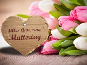 Ein Herz aus Karton mit der Aufschrift :Alles gute zum Muttertag. Daneben sind weisse und rosafarbene Tulpen.