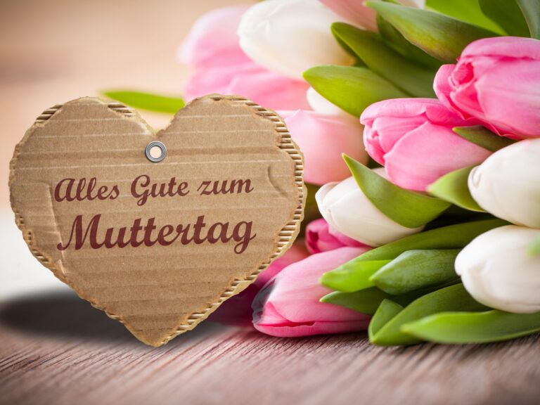 Ein Herz aus Karton mit der Aufschrift :Alles gute zum Muttertag. Daneben sind weisse und rosafarbene Tulpen.
