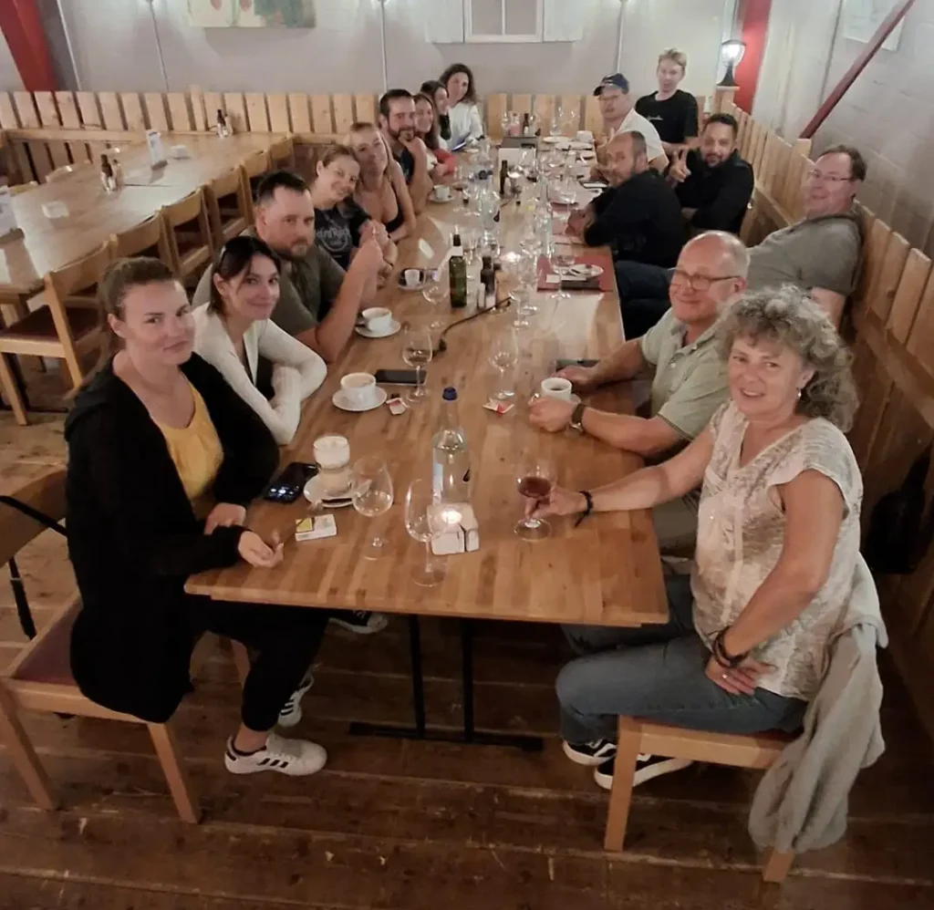 Das ganze Team von der Traimmo AG sitzt gemütlich am Holztisch bei Tischpizza und Getränken.